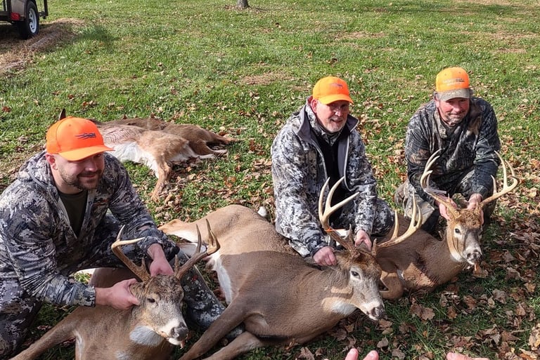 Three hunters posing in a field with multiple harvested whitetail bucks.