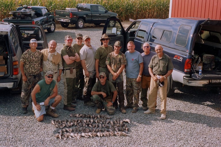 Large group of hunters posing with their harvest and gear in front of parked trucks.