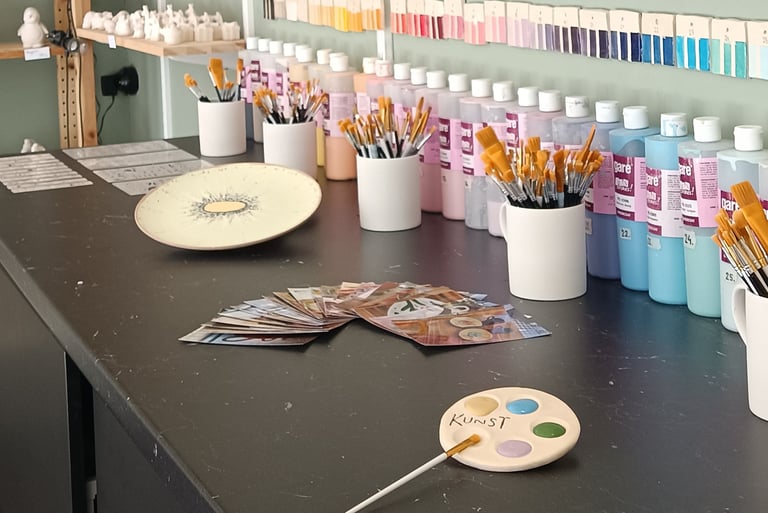 Pottery studio workbench with paintbrushes, ceramic glazes, and unpainted pottery figurines.