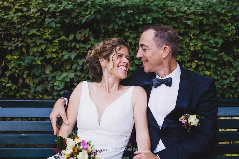 Bride and groom sitting on a blue park bench.