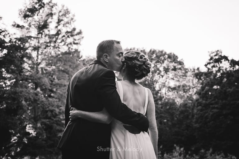 Groom kissing bride on the side of her head.