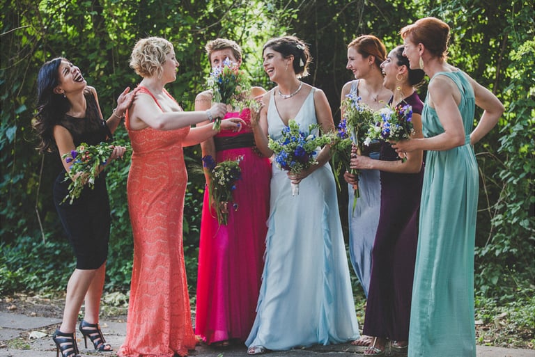 A laughing bride surrounded by bridesmaids  in colourful dresses.