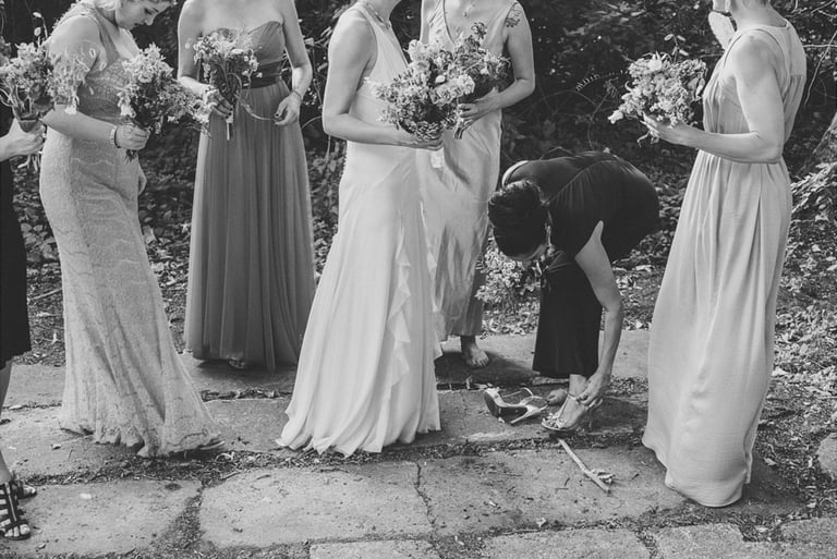 A bridesmaid fixing her shoe strap surrounded by other bridesmaids.
