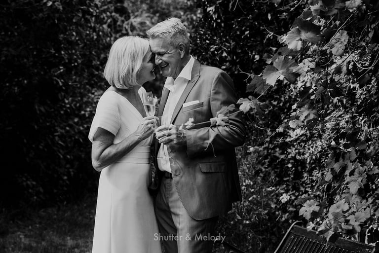 An older happy couple toasting in a garden.