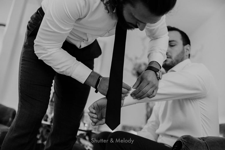 Best man putting cuff links on the groom's sleeves..