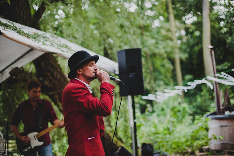 Groom in a red suit and a hat singing.