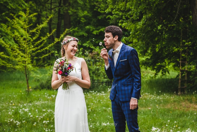 Bride smiling with closed eyes as groom blowing into a dandelion.
