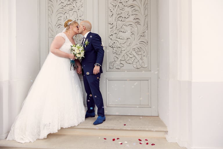 Bride and groom kissing in front of a carved door.
