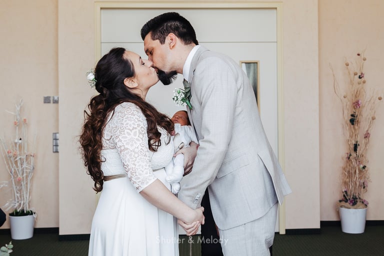 Bride and groom kissing and holding a baby.