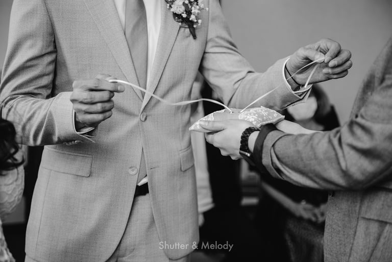 Groom untying a ribbon holding wedding rings.