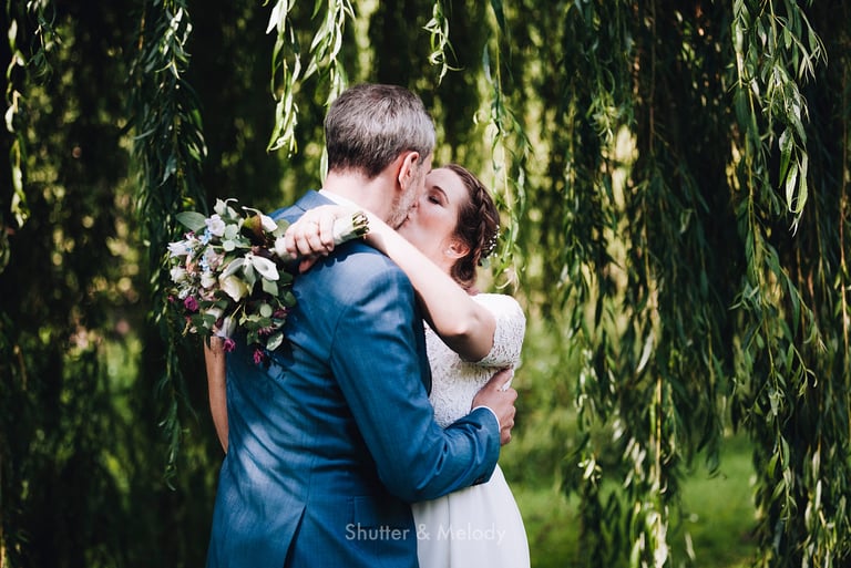 Bride kissing groom underneath a willow tree.