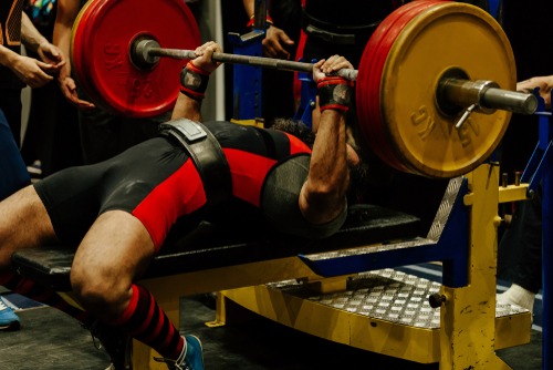 Professional powerlifter performing a heavy bench press with weighted plates during a competition.