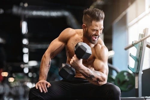 A muscular man performing a bicep curl with a heavy dumbbell in a gym for bodybuilding strength training.