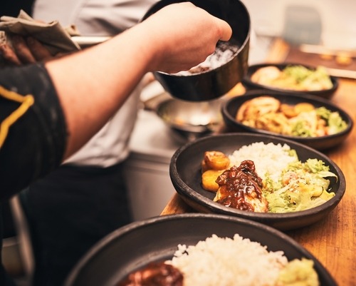 Professional chef plating gourmet chicken and rice bowls with salad in a commercial kitchen.
