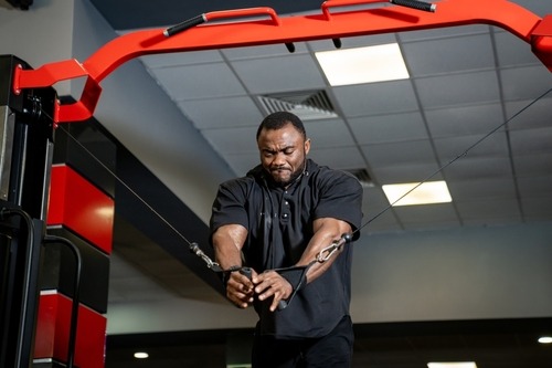 Muscular man performing a cable chest fly workout on a gym machine for strength training.