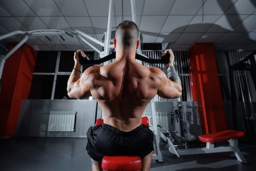 A muscular bodybuilder performs a lat pulldown exercise to strengthen his back muscles in a gym.