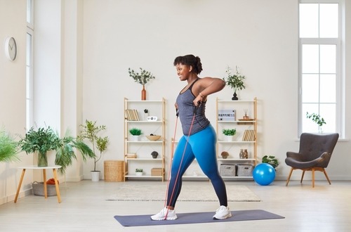 Smiling woman performing upright rows with a resistance band during an indoor home workout.