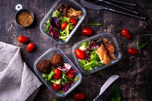 Glass meal prep containers with healthy salads, roasted chicken, and falafel on a dark wooden table.