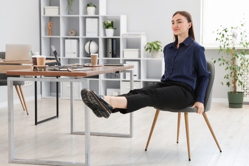 A woman performing leg extensions as office exercises while sitting at her desk in a modern workspace.