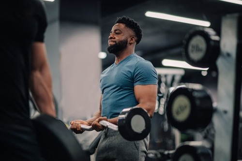 A man performing bicep curls with a barbell during a strength training workout in a modern gym.