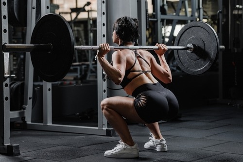 Athletic woman performing a heavy barbell back squat in a gym power rack for strength training.
