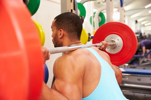 Muscular man performing heavy barbell squats with red weights at a fitness gym.