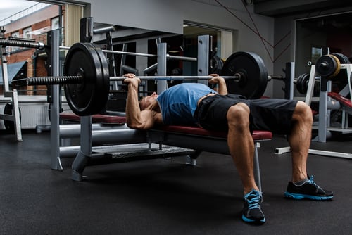 Muscular man performing a barbell bench press exercise for chest strength training in a gym.