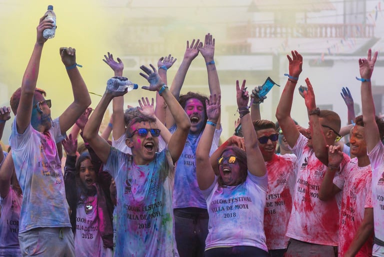 Excited people covered in colorful powder celebrate at a Holi color festival event.