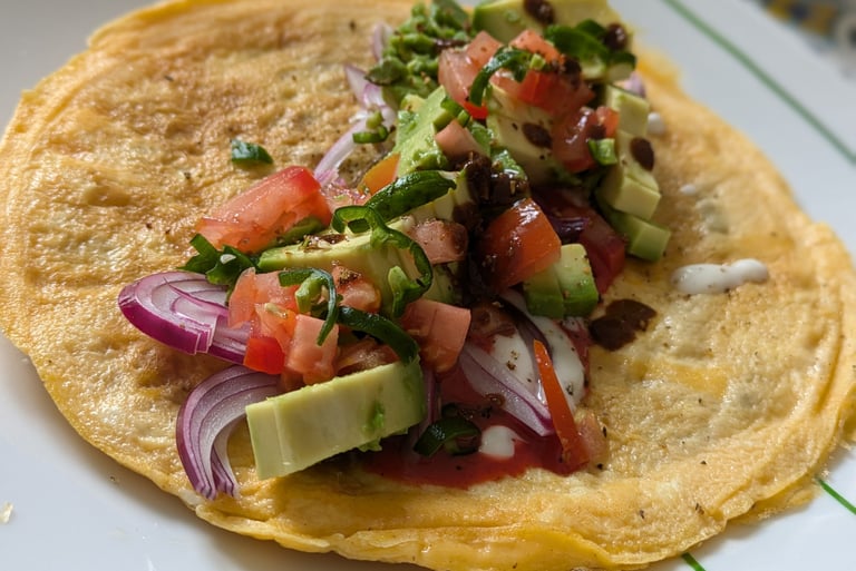 An Indian Kathi Roll with omelet layered on top of a Lacha Parantha and a filling of avocado, red onion and tomatoes 
