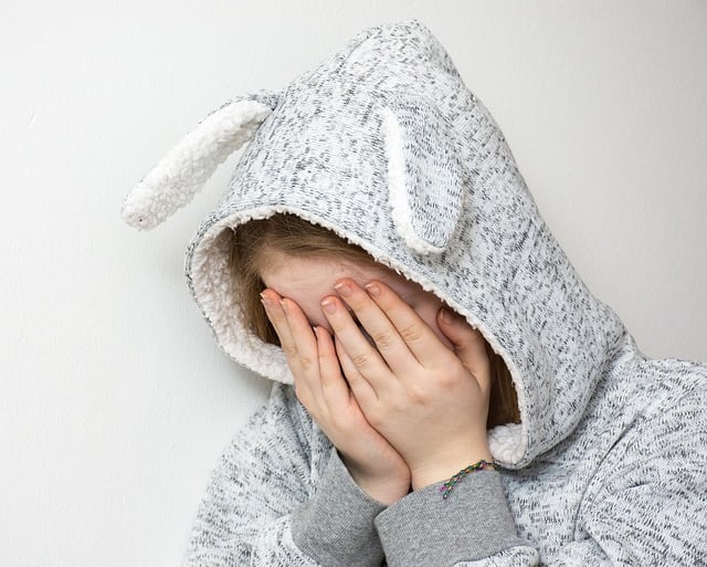 una niña con un suéter gris con orejas de conejo y una sudadera con capucha con la cara tapada