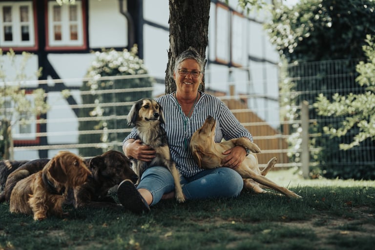 Hundetrainerin Marion Lindhof sitzt mit ihren Hunden im Garten vor einem Baum.