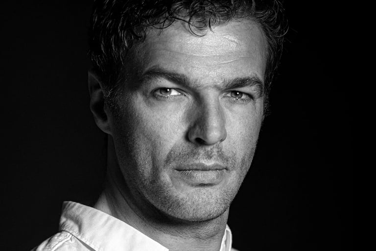 Schwarz-Weiß-Porträt eines Mannes mit dunklen Haaren, der direkt in die Kamera blickt.