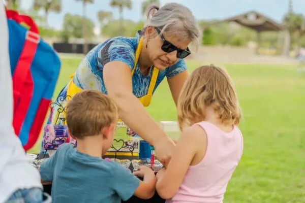 older woman helping two children with arts and craft activities