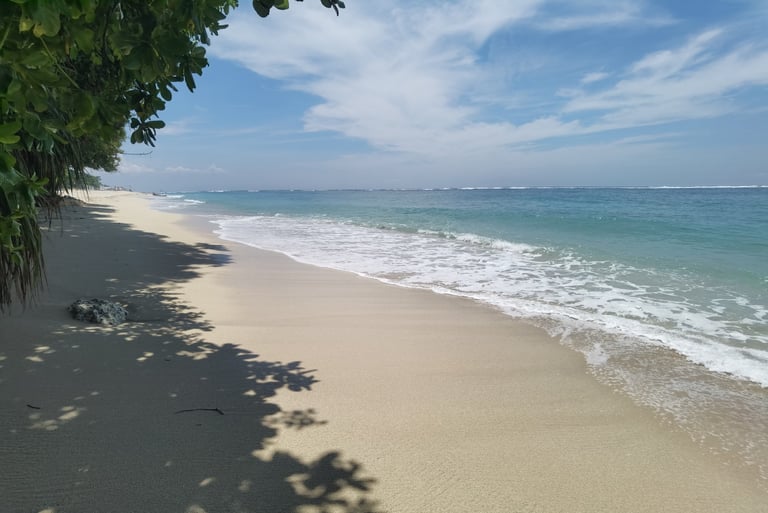Pristine white sand beach with turquoise ocean waves under  blue sky with tropical tree shadows Bali