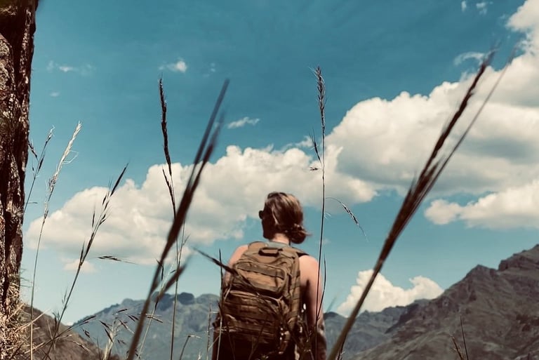 A hiker with a backpack sitting on a stone wall overlooking scenic mountain under a blue sky in Peru