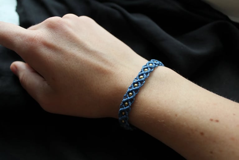 Eine Hand trägt ein dunkelblaues geknüpftes Makramee Armband mit goldenen Perlen