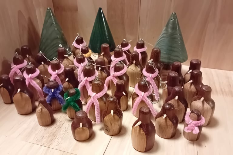 A group of turned wooden penguins in dark wood with light front and light beak. Some wearing pipecleaner scarfs