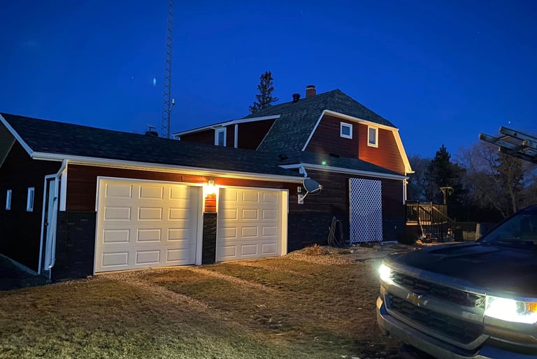 Red residential barn-style house with a two-car garage illuminated at night with a truck parked in the driveway.