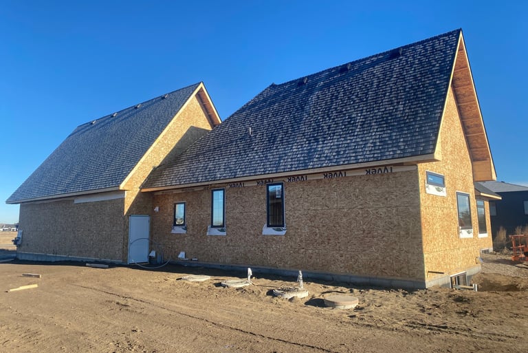 New house construction with plywood sheathing, dark shingle roof, and installed windows under a clear blue sky.