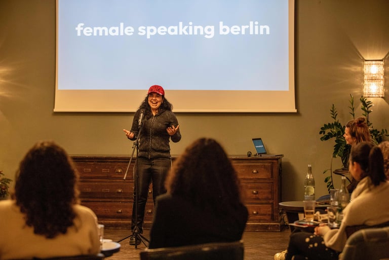 Smiling confident woman, wearing a cap, talking behind microphone in front of screen showing logo.