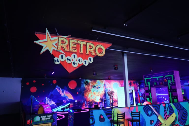 Indoor retro mini golf course featuring neon blacklight wall murals and vintage signs.