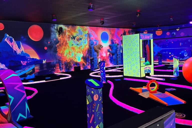 Indoor blacklight mini golf course featuring neon tracks, cosmic murals, and retro arcade vibes.