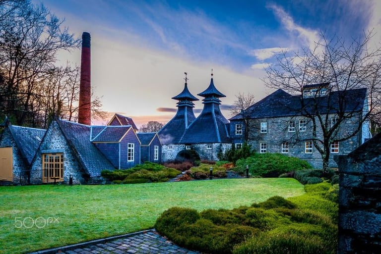 Historic Scottish whisky distillery with pagoda roofs and tall chimney at sunset.