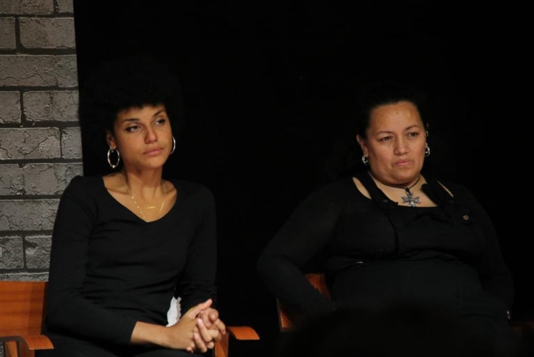 Dos mujeres actrices migrantes sentadas en el escenario en un banco de una habitación