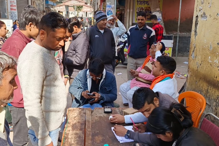 A crowded outdoor information booth in India with people gathering at a desk to complete official forms.