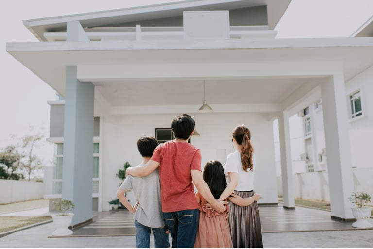 Familia abrazada contemplando su vivienda de color blanco