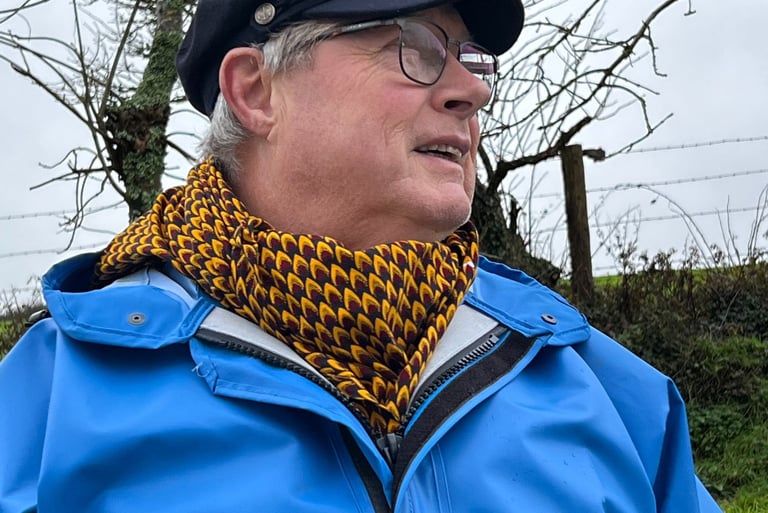 A weathered faced man with waterproof coat and captains hat wearing a noseknot bandane to keep warm