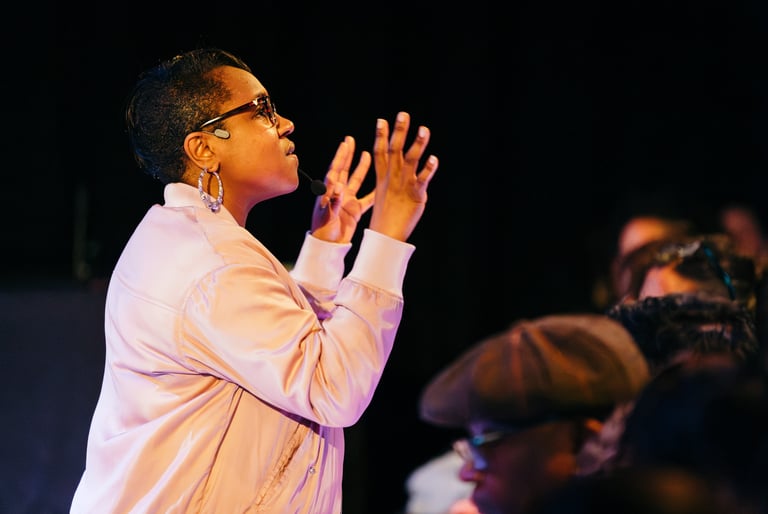 a Black woman in a pink jacket and glasses among audience