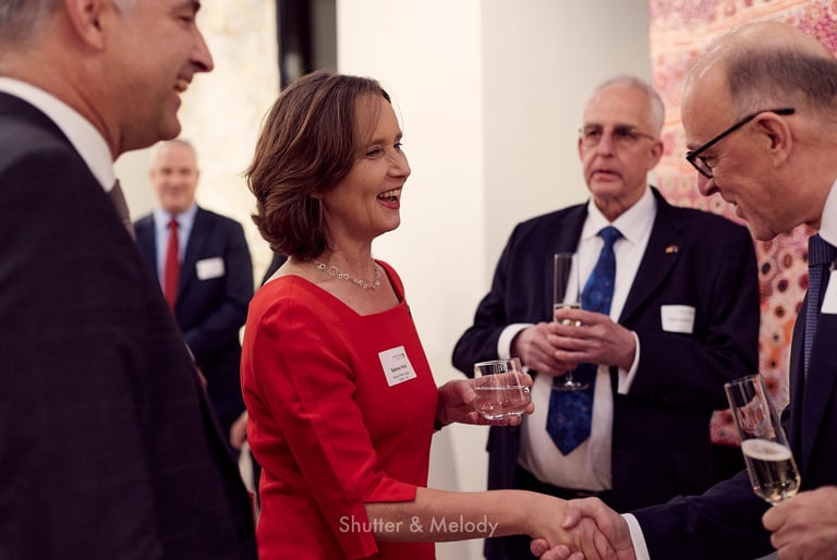 Sabine Pittrof in einem roten Kleid schüttelt einem Gast die Hand.
