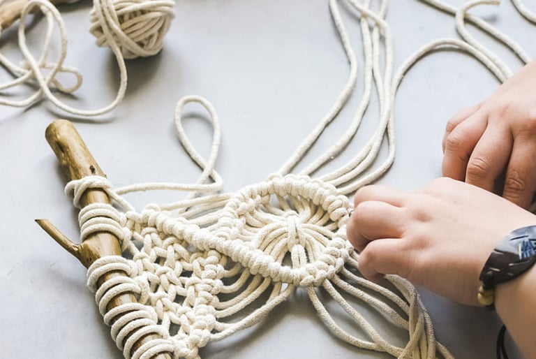 Manos creando un tapiz de macramé hecho a mano, entrelazando cuerda de algodón natural